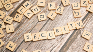 Scrabble tiles spell "SECURITY" on a wooden surface, surrounded by scattered letters. The scene conveys a sense of focus amidst chaos.